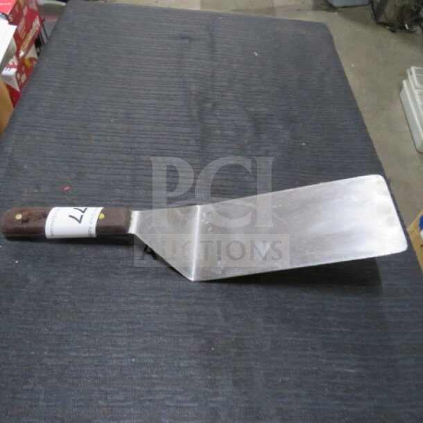 Stainless steel XXL hamburger turner with a wooden handle, slightly worn condition, auction tag visible on handle.