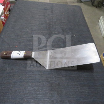 Stainless steel XXL hamburger turner with a wooden handle, slightly worn condition, auction tag visible on handle.