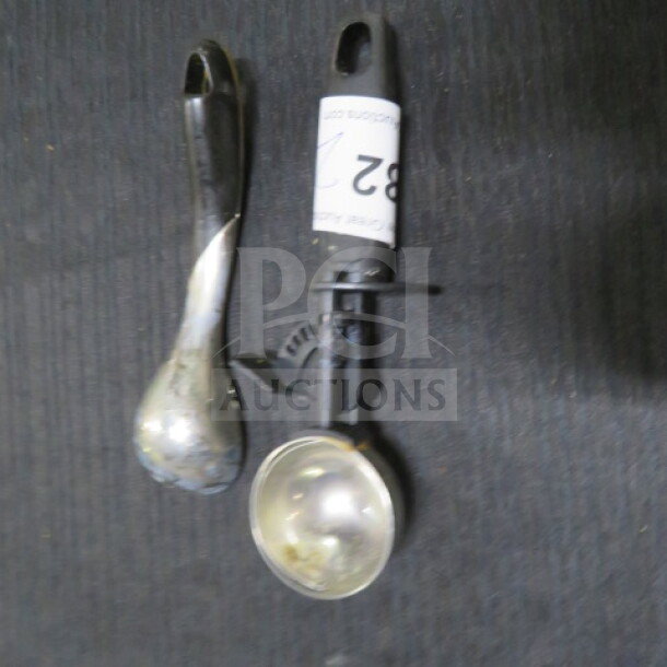 Assorted utensils, including a metal ice cream scoop and a spoon, both in used condition. Item labeled "82".