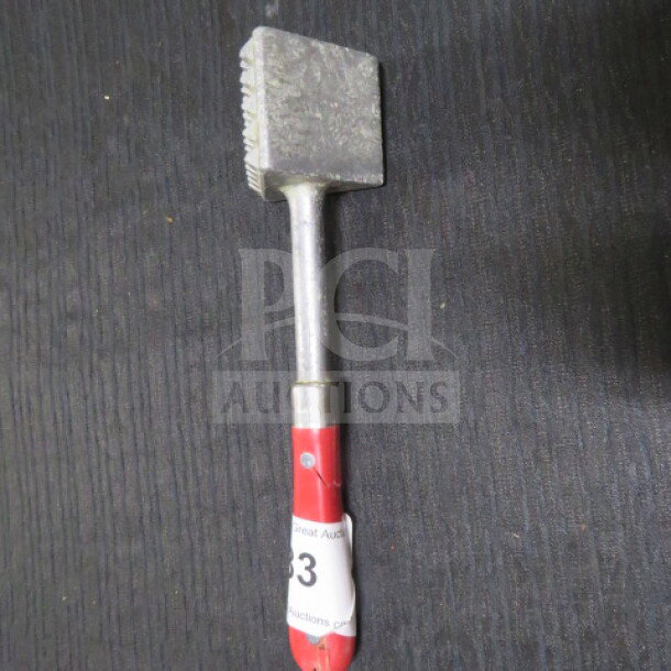 Metal meat tenderizer with a textured head and a red handle, showing wear. Auction tag attached to handle.