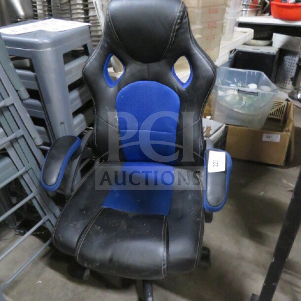 Black and blue gaming chair on casters, with ergonomic design and padded armrests. Some visible wear on seat and back.