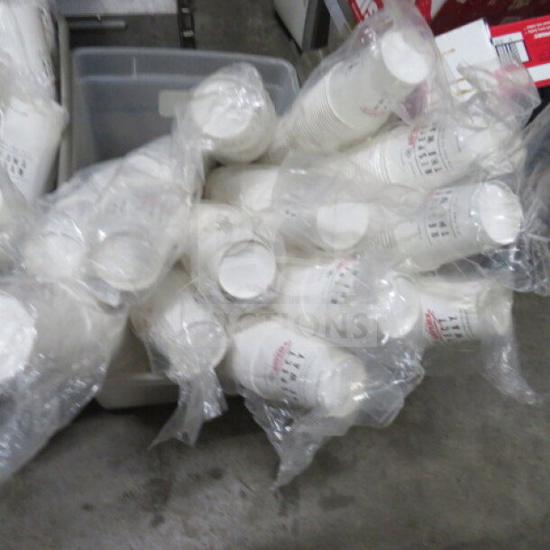 Lot of white paper cups in clear plastic wrapping, stacked and placed in a storage bin. Ideal for bulk use.