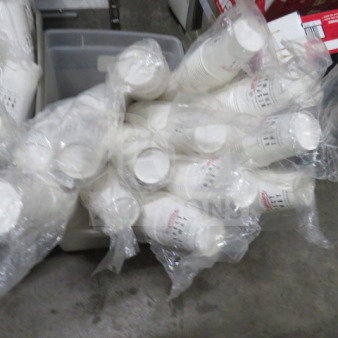 Lot of white paper cups in clear plastic wrapping, stacked and placed in a storage bin. Ideal for bulk use.