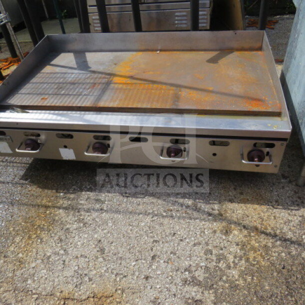 Wolf natural gas griddle with three control knobs, stainless steel surface, and visible wear from use.