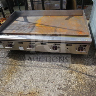 Wolf natural gas griddle with three control knobs, stainless steel surface, and visible wear from use.