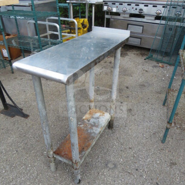 Stainless steel table with under shelf, 12x30x34.5 inches, showing surface wear and rust on lower shelf, sturdy condition.