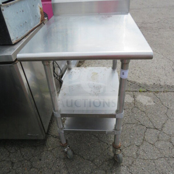 Advance Tabco stainless steel table, model KMS-302, features two under shelves, backsplash, and casters. Size: 24x30x41.5 inches.