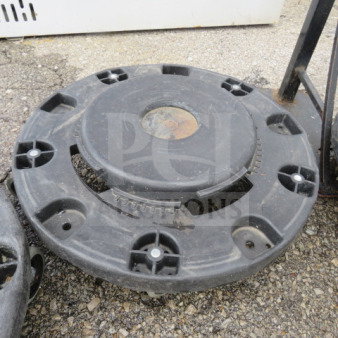 Round black dolly for bin or trash can, sturdy plastic, shows signs of wear, includes multiple wheel fittings.