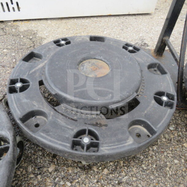 Black plastic ingredient bin/trash can dolly in used condition, featuring multiple wheel sockets and central support, lying on pavement.