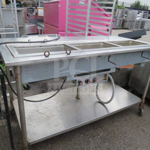 Stainless steel steam table with three wells, SS undershelf, on casters, measures 72x36x40 inches, slight wear visible.