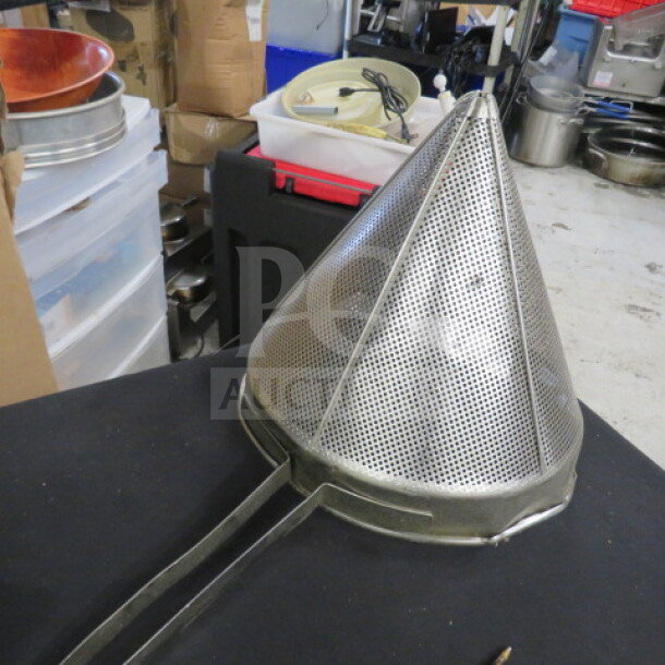 Stainless steel cone strainer, perforated design, with extended handle, in used condition on a black surface.