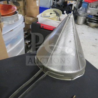 Stainless steel cone strainer, perforated design, with extended handle, in used condition on a black surface.