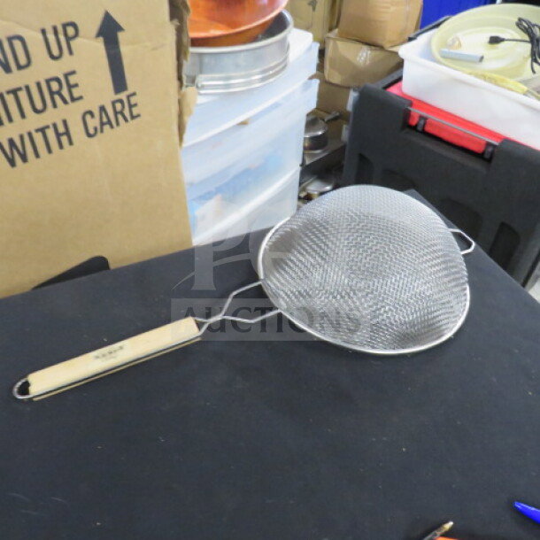 Stainless steel mesh strainer with wooden handle, good condition. Ideal for sifting and straining in kitchen tasks.