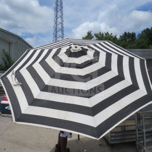 Black and white stripe patio umbrella, round canopy, metal pole, visible under blue sky, in good condition.