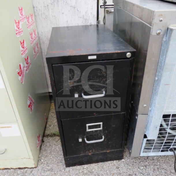 Black metal 2-drawer file cabinet, showing wear and scratches. Features silver handles and a lock on the top drawer.