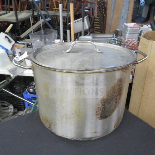 Stainless Steel 40qt Stock Pot with Lid, Model SST-40, showing signs of wear, ideal for large cooking tasks.
