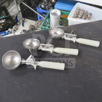 Three gray-handled dishers on a table, stainless steel scoops, used condition, varying sizes. Industrial background.