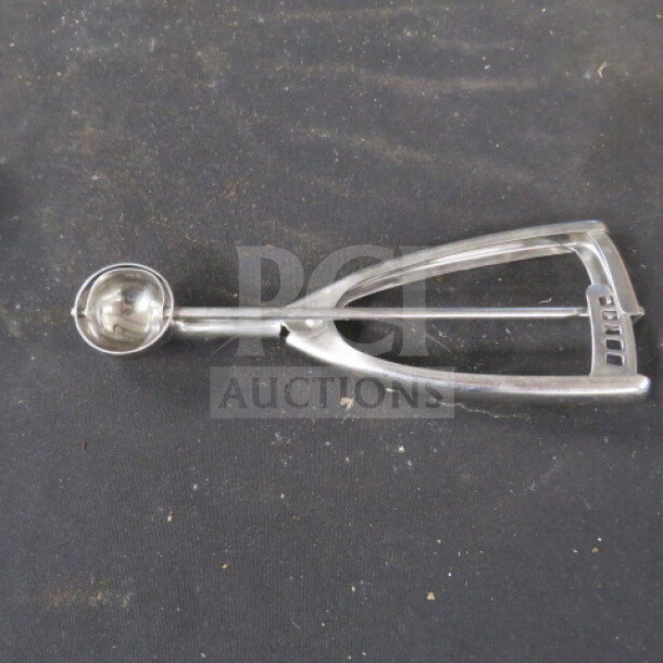 Stainless steel disher with a spring mechanism on a dark background, showing slight wear. Ideal for scooping.