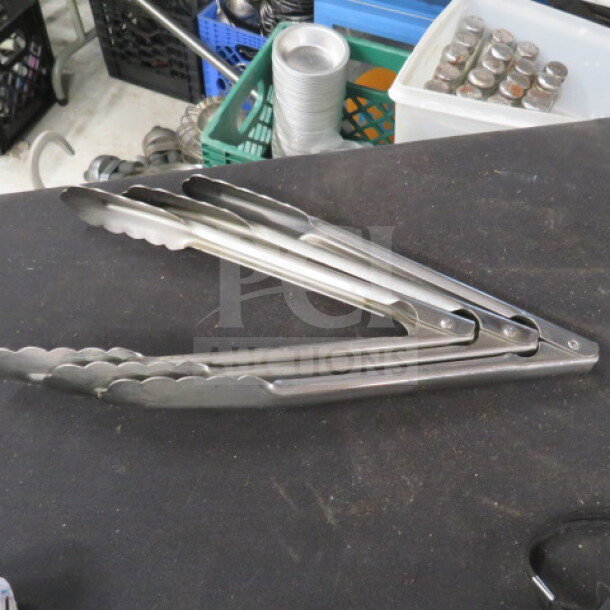 10-inch stainless steel tongs, lightly used, serrated edges, labeled "3XBID," on display table.