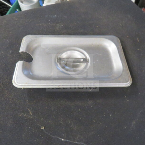 Stainless steel 1/9 size lid with utensil notch, handle, and 3XBID marking. Slight wear visible.