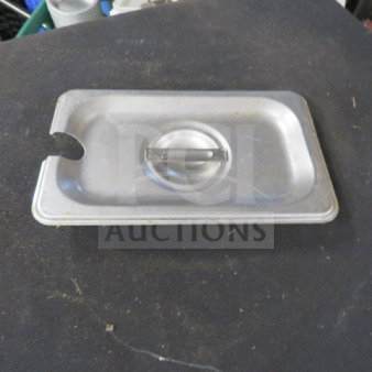 Stainless steel 1/9 size lid with utensil notch, handle, and 3XBID marking. Slight wear visible.