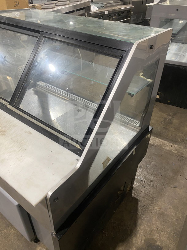 Glass display case with angled front, stainless steel base, and shelving. Visible wear. Ideal for showcasing items.