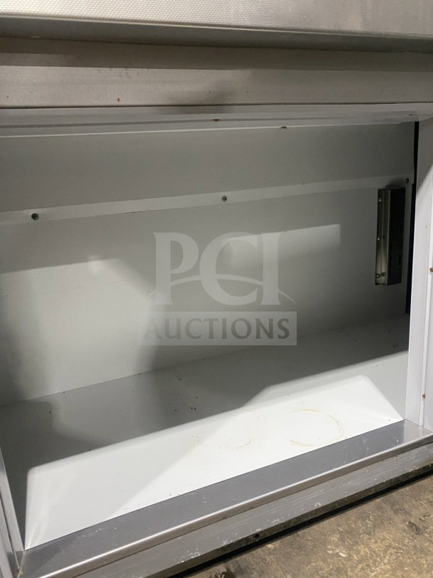 Empty white storage compartment with metal frame, visible wear and scuffs on surfaces, no labels or markings.