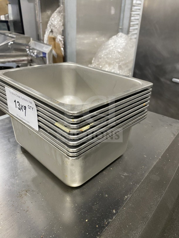 Stack of commercial stainless steel half-size hotel food pans, used, with label indicating 13x9 quantity.