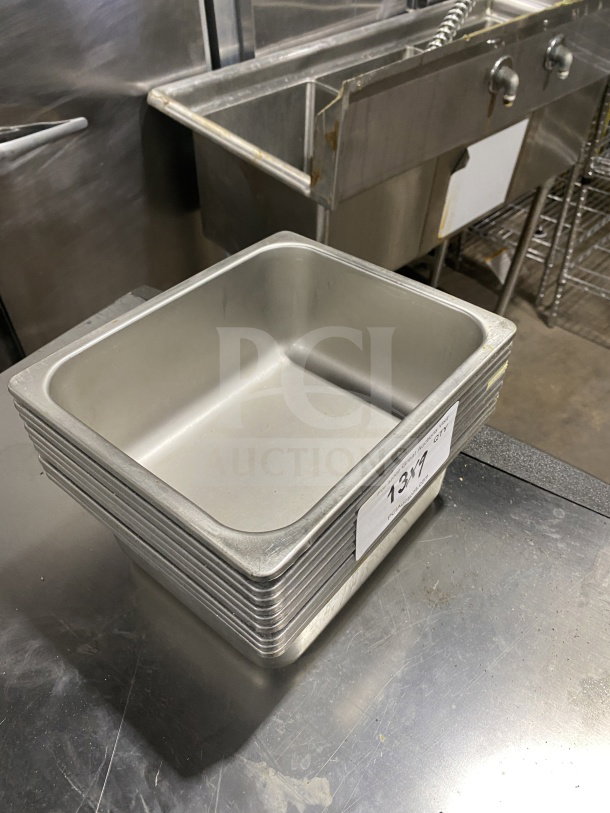 Commercial stainless steel half-size hotel food pans, stack of nine, used condition with label "13X9" visible.