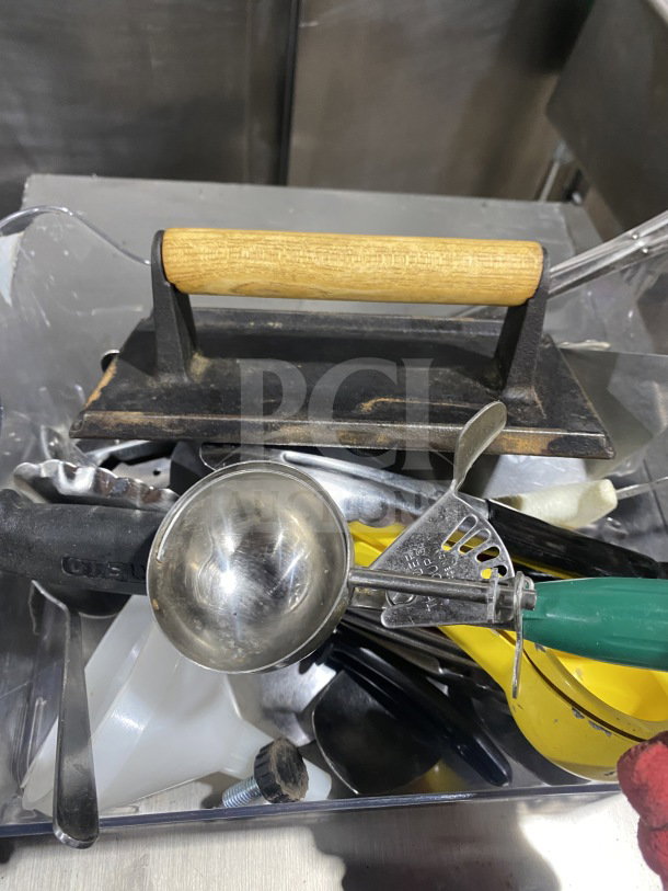 Assorted commercial kitchen smallwares and utensils, including a metal griddle press and ice cream scooper, used condition.