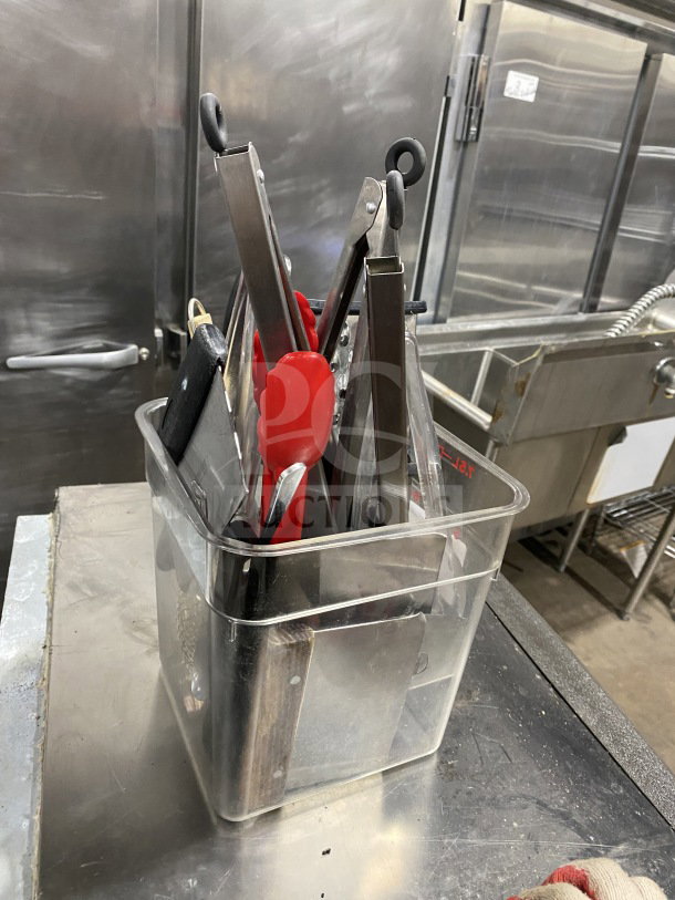 Commercial kitchen smallwares and prep utensils lot in plastic container; includes tongs, spatulas, and knives.