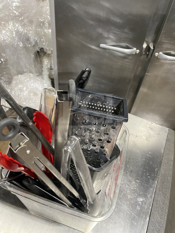 Commercial kitchen smallwares and prep utensils lot in plastic container, includes tongs, grater, and scoop. Good condition.