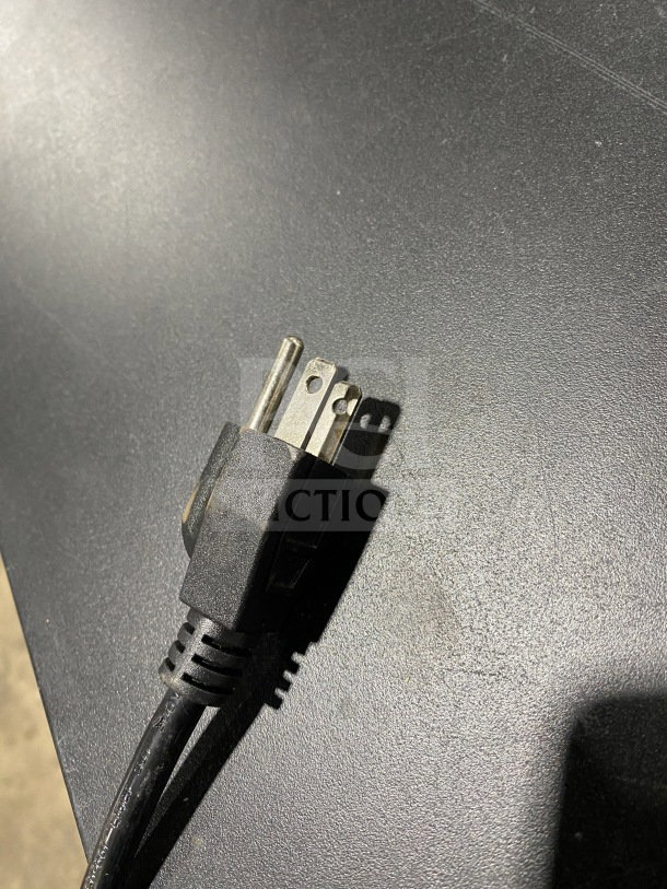 Close-up of a black power plug against a textured surface, highlighting its three-prong design.