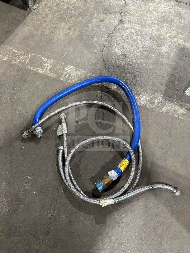Metal and blue rubber hoses, each with brass fittings and industrial connectors, laid on a concrete floor.