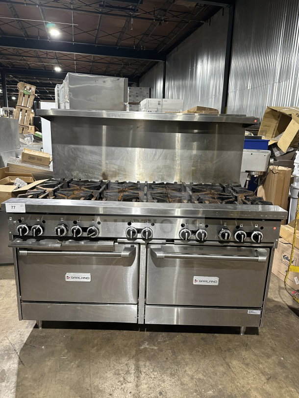 Garland commercial stainless steel 10-burner gas range with double oven, backsplash, and wire rack. Used condition, on legs.
