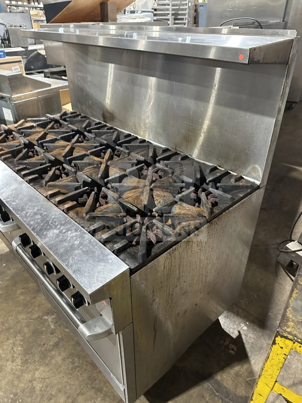 Garland stainless steel 10-burner gas range with double oven, backsplash, and wired rack. Used condition on legs.