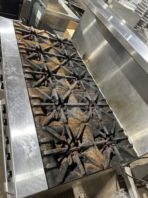 Garland commercial stainless steel 10-burner gas range with double oven, backsplash, and wired oven rack, on legs.