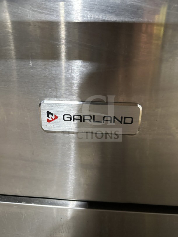Garland stainless steel 10-burner range with double oven combo, backsplash, and wired oven rack. Brand logo visible.