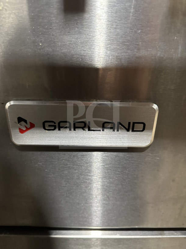 Garland stainless steel gas-powered range with 10 burners, double oven, backsplash, wired rack, and legs.
