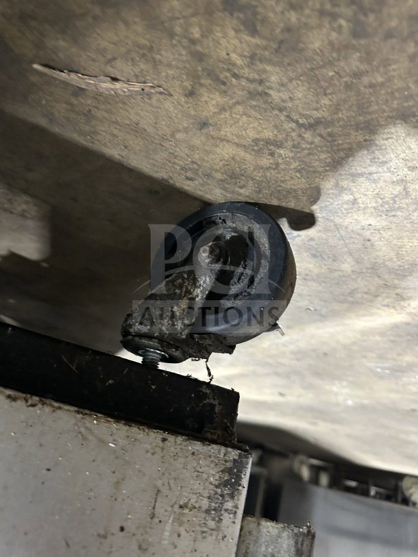 Close-up of a caster wheel under a True T-49 commercial refrigerator, showing signs of wear and dirt accumulation.