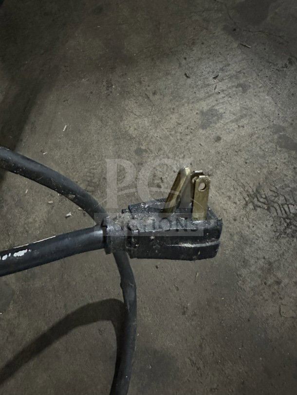 A worn black power plug on a dusty floor, part of the True Model T-49 refrigerator wiring.