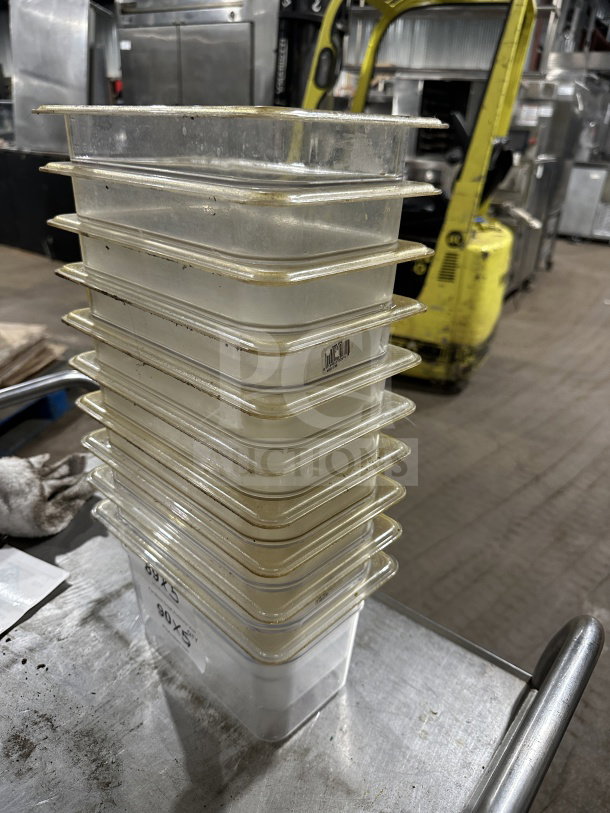 Stack of Cambro commercial polycarbonate translucent full-size food pans on metal surface, used condition.