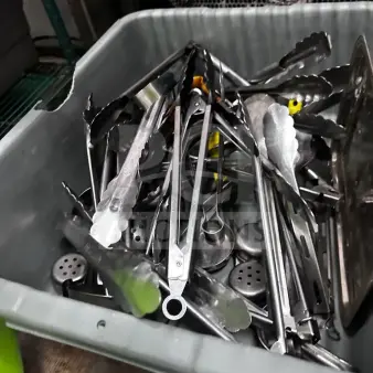 Mixed commercial kitchen utensil lot in gray container, featuring tongs, spatulas, ladles, and serving tools. Well-maintained.