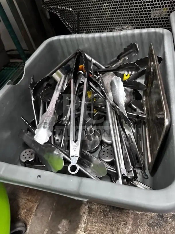 Mixed commercial kitchen utensil lot in a bin, including tongs, spatulas, and ladles, well-maintained for restaurant use.