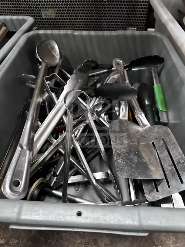Mixed commercial kitchen utensil lot in two containers, featuring tongs, spatulas, ladles, and serving tools. Well-maintained condition.
