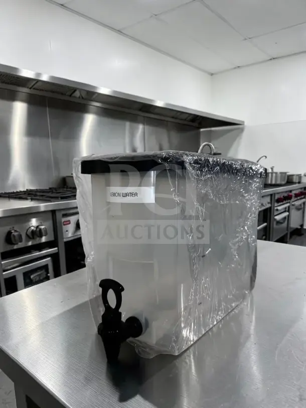Like-new plastic cold juice dispenser with spigot, labeled "Lemon Water," in a kitchen setting, wrapped for protection.