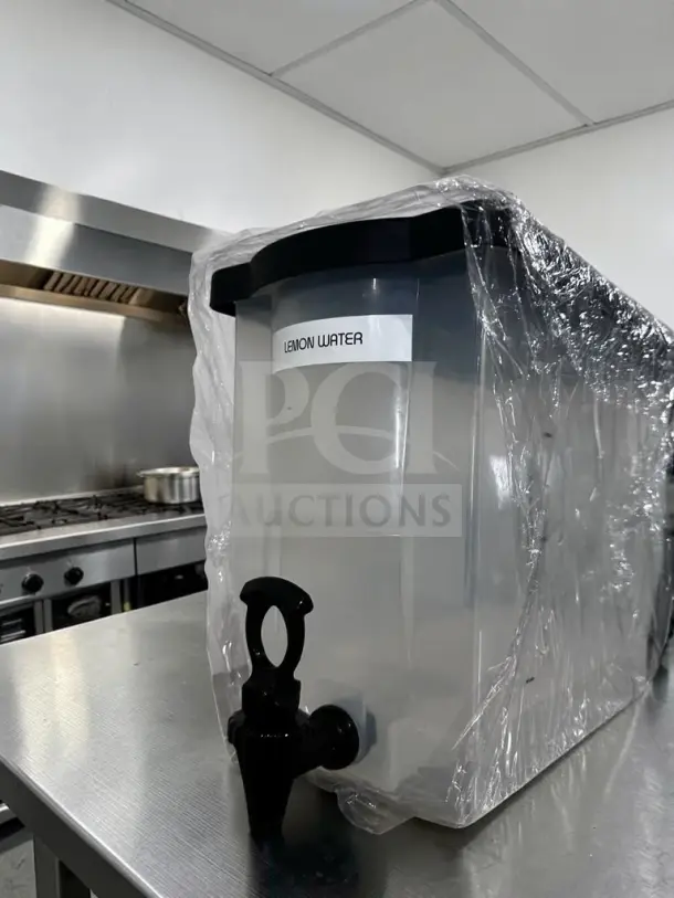 Like-new plastic cold juice dispenser with spigot, labeled "Lemon Water," wrapped in plastic, countertop-ready.