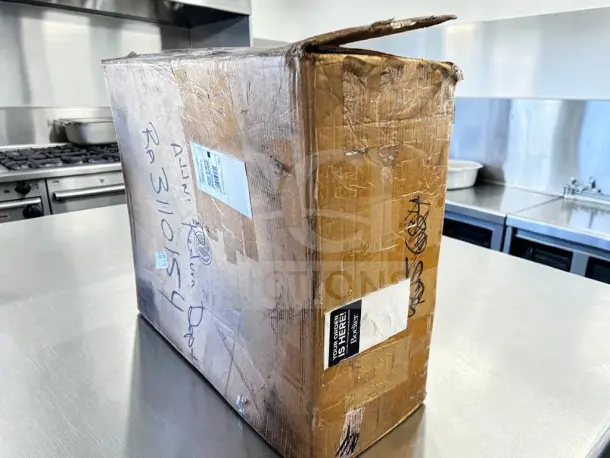Sealed box on kitchen counter labeled "Wells 5P-MOD200TDM Two-Well Top-Mount Food Warmer." Box shows shipping labels.