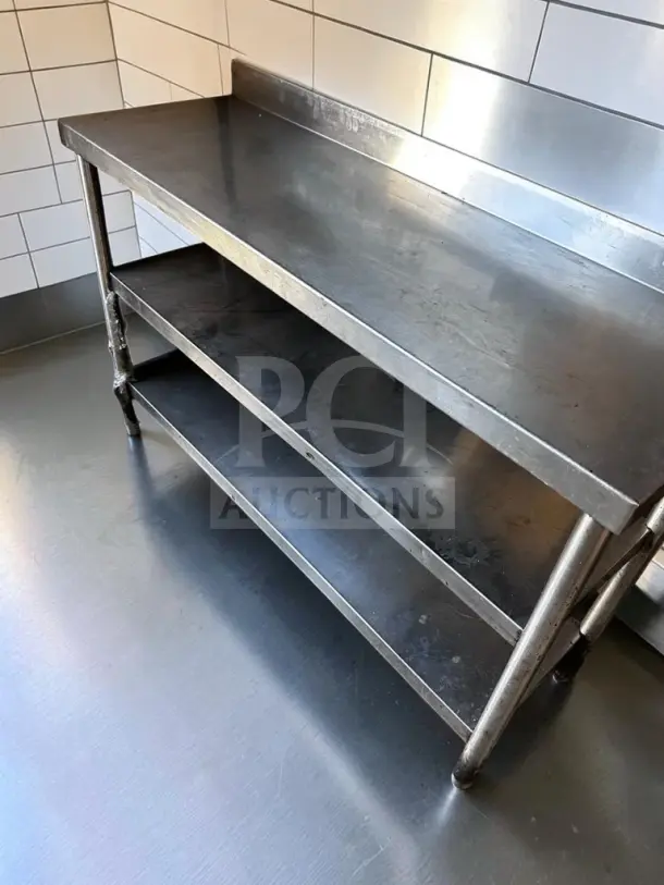 Stainless steel commercial work table, 55" × 17", with two undershelves and a backsplash. Model UNB-S-TBL-1353, excellent condition.