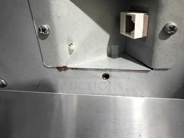 Close-up of APG Vasario VB452-BL1313 electronic POS cash drawer, showing RJ connection port and metal casing with visible scuff marks.